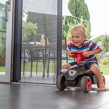 Ein Jung fährt mit einem Bobby-Car von der Terrasse ins Haus